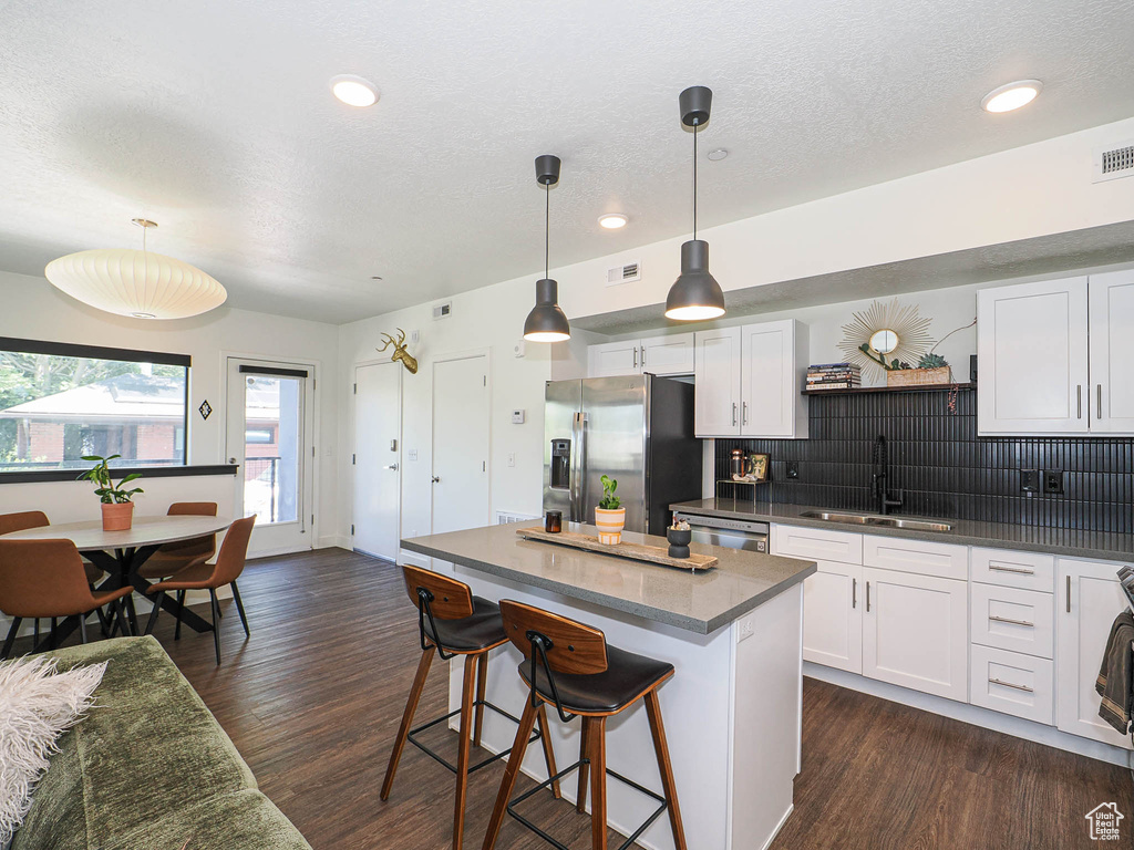 Kitchen featuring stainless steel appliances, a breakfast bar area, white cabinetry, a kitchen island, and dark wood-style floors