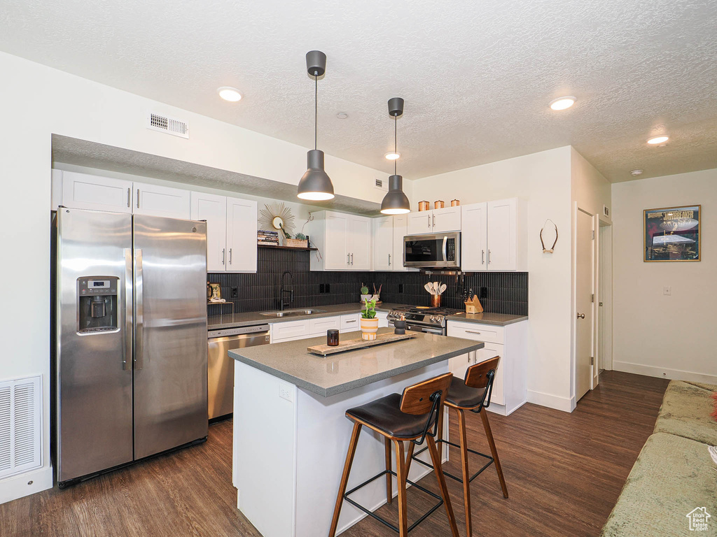 Kitchen with stainless steel appliances, dark wood-style flooring, decorative backsplash, white cabinetry, and a textured ceiling