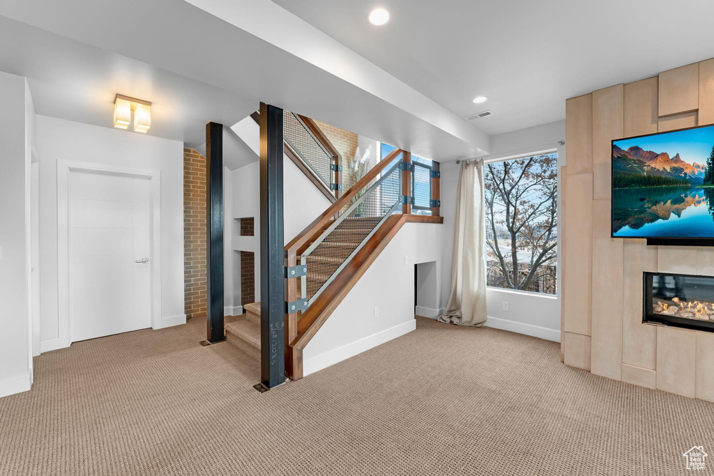Unfurnished living room with light colored carpet, a large fireplace, stairs, and recessed lighting