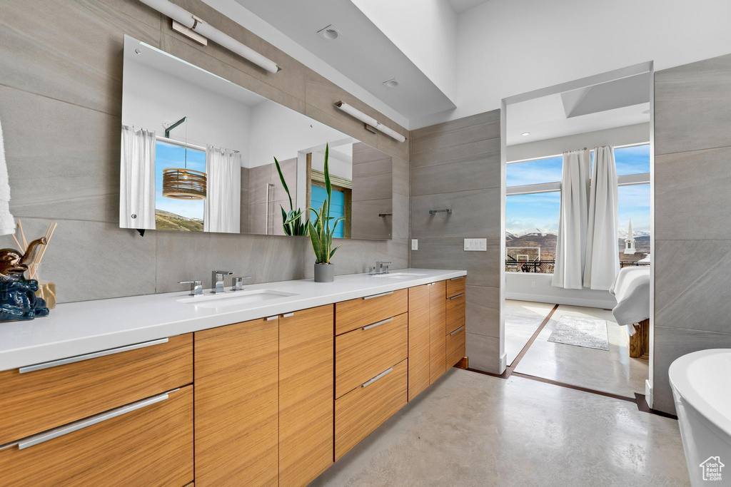 Full bathroom with a freestanding tub, double vanity, finished concrete flooring, healthy amount of natural light, and tile walls