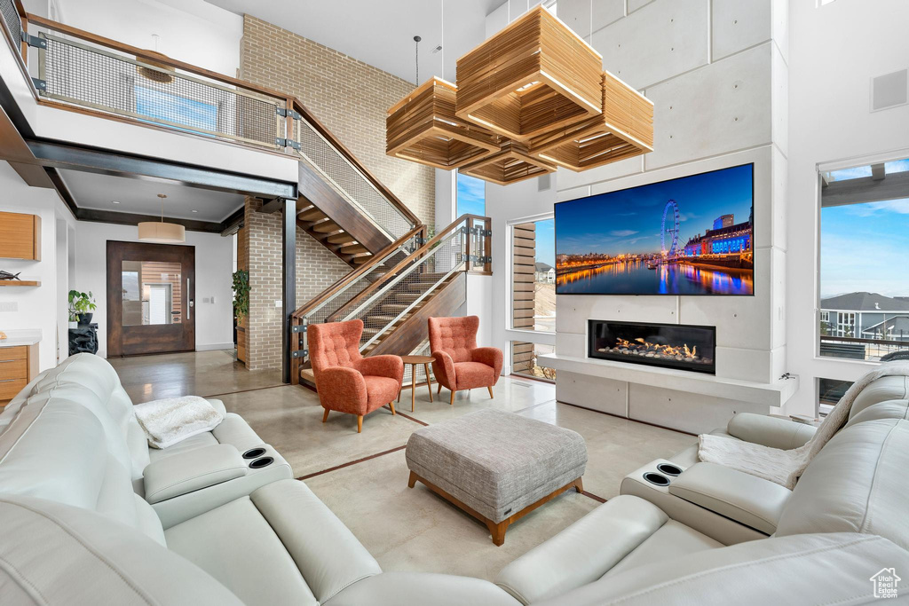 Living room featuring a towering ceiling, stairway, finished concrete floors, a glass covered fireplace, and healthy amount of natural light