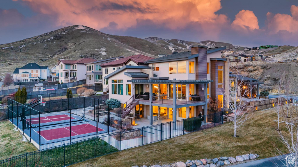 Back of property at dusk featuring a tennis court, stairway, a mountain view, and a patio