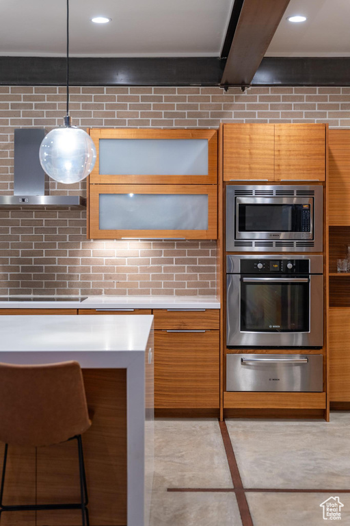 Kitchen with stainless steel appliances, a warming drawer, wall chimney exhaust hood, light countertops, and backsplash