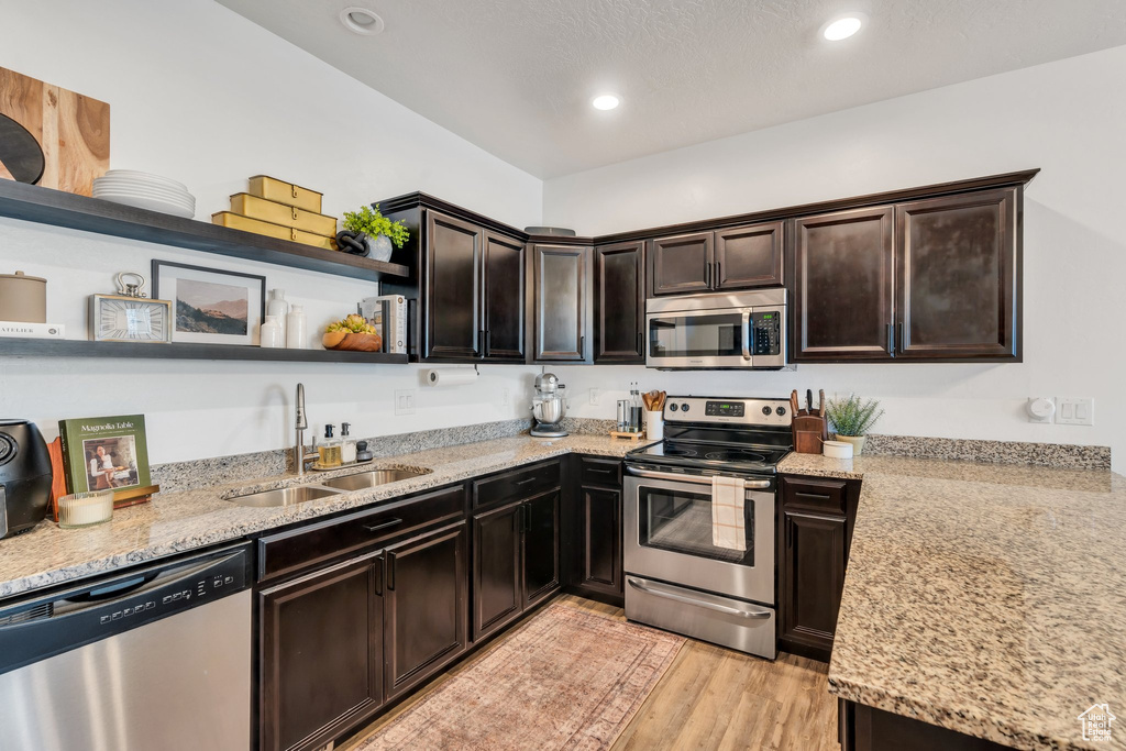 Kitchen featuring appliances with stainless steel finishes, open shelves, dark brown cabinets, light stone counters, and light wood-style flooring