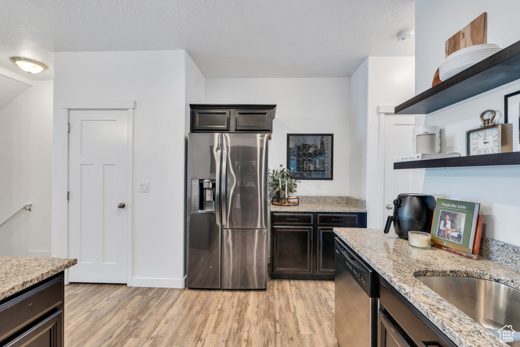 Kitchen with appliances with stainless steel finishes, open shelves, light wood finished floors, and light stone counters
