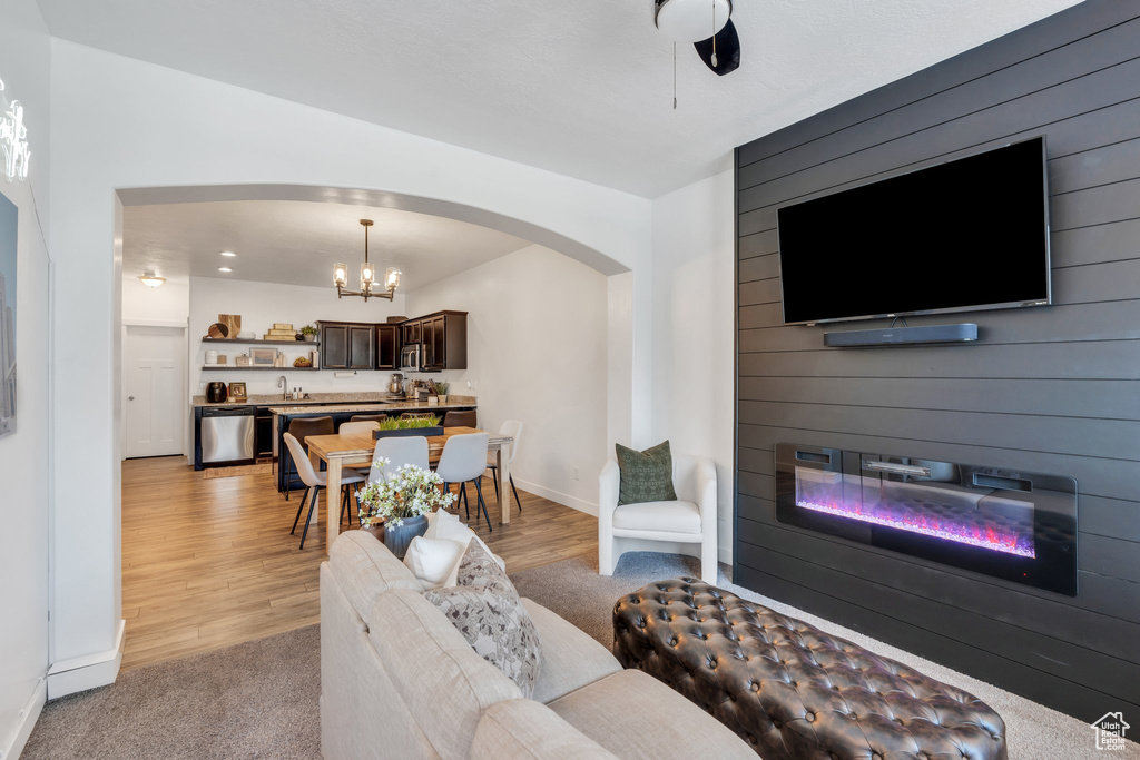 Living room with arched walkways, a large fireplace, a chandelier, and light wood-style floors
