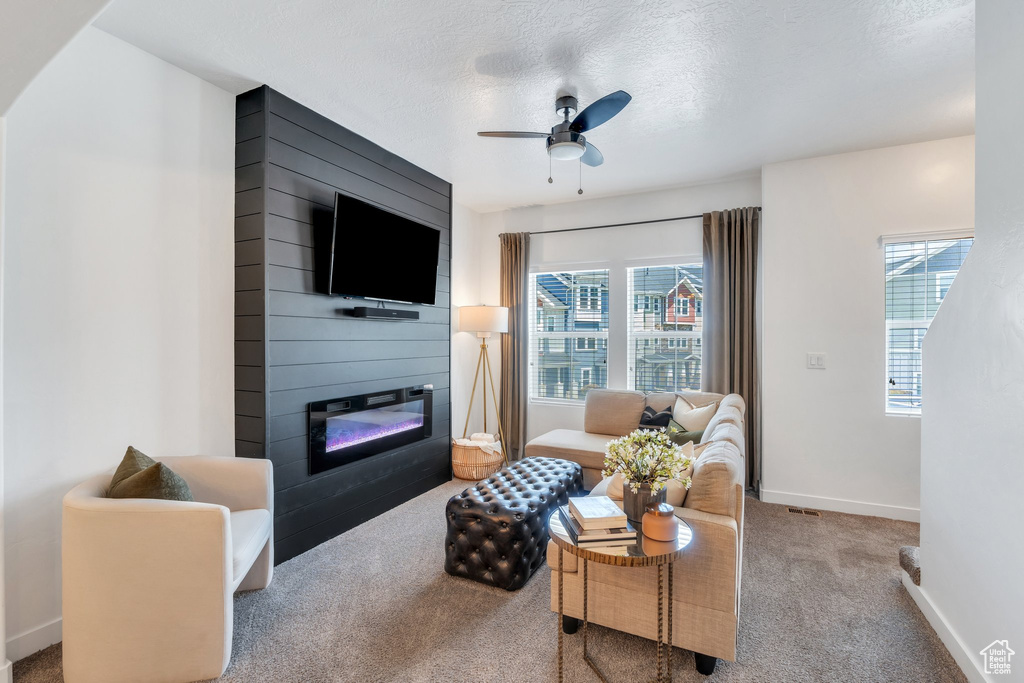 Carpeted living room with a fireplace, ceiling fan, healthy amount of natural light, and a textured ceiling