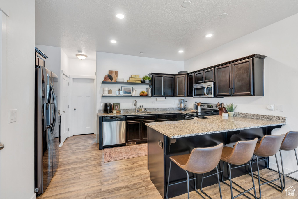 Kitchen with stainless steel appliances, a peninsula, open shelves, light wood-style flooring, and dark brown cabinets