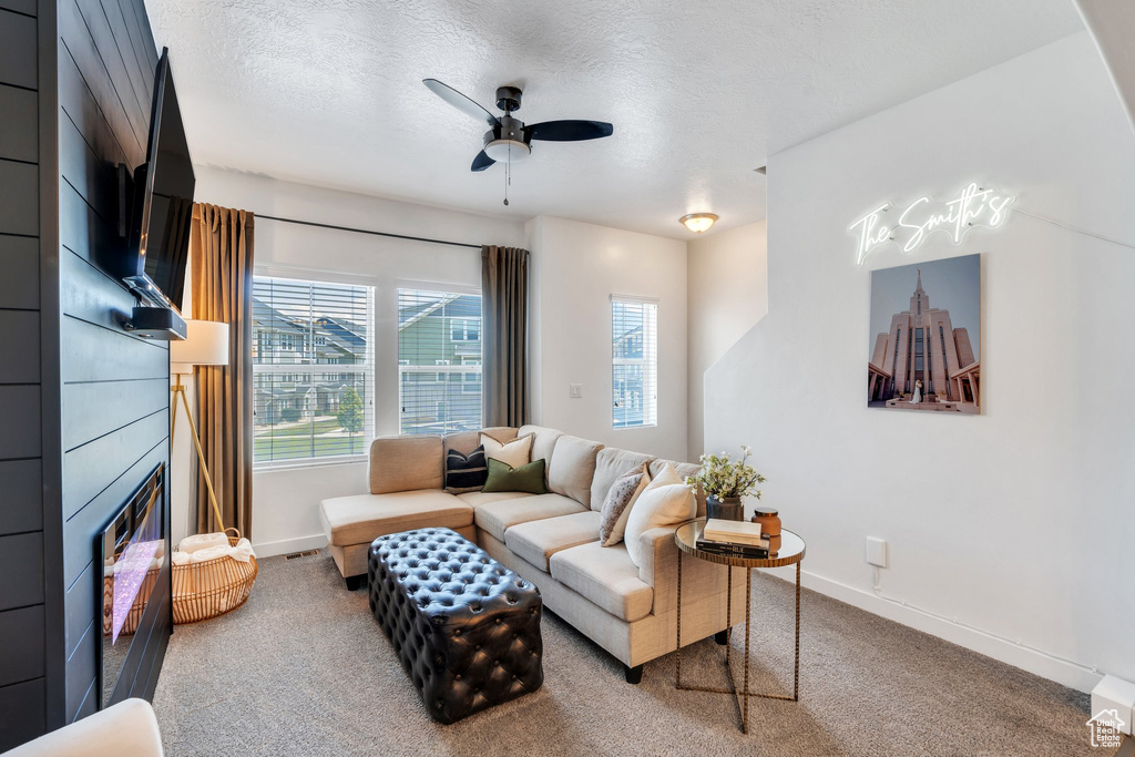 Living area featuring carpet, ceiling fan, a textured ceiling, and a large fireplace