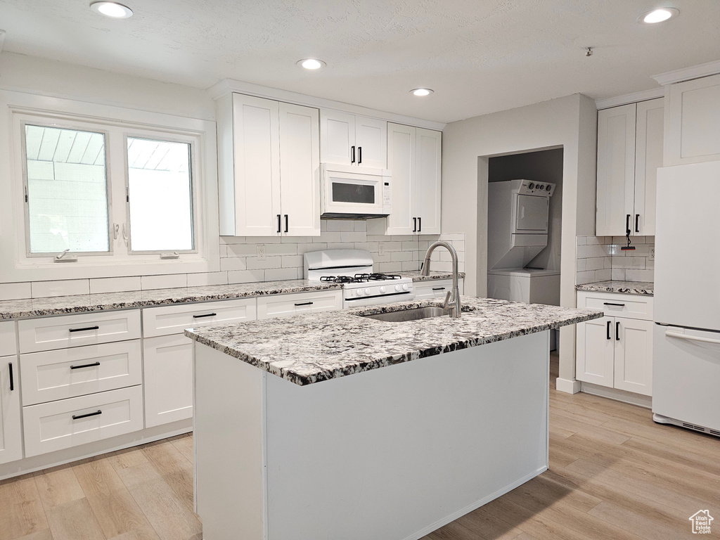 Kitchen featuring white appliances, stacked washer and clothes dryer, light wood finished floors, light stone countertops, and recessed lighting
