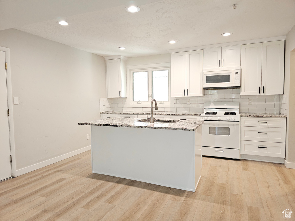 Kitchen featuring white appliances, light wood-style floors, tasteful backsplash, light stone counters, and white cabinets