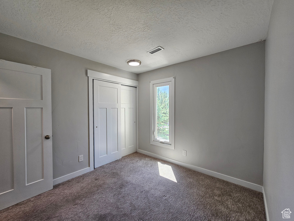 Unfurnished bedroom featuring carpet flooring, a textured ceiling, and a closet