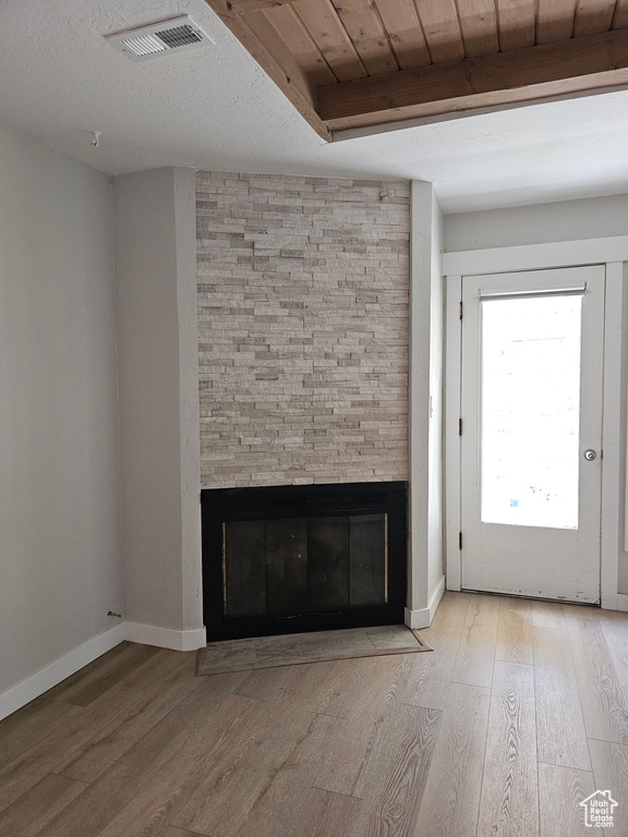 Unfurnished living room featuring a fireplace, wood finished floors, and a wooden ceiling with exposed beams