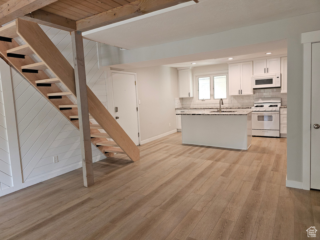 Kitchen featuring white appliances, backsplash, light wood-style floors, white cabinetry, and a kitchen island