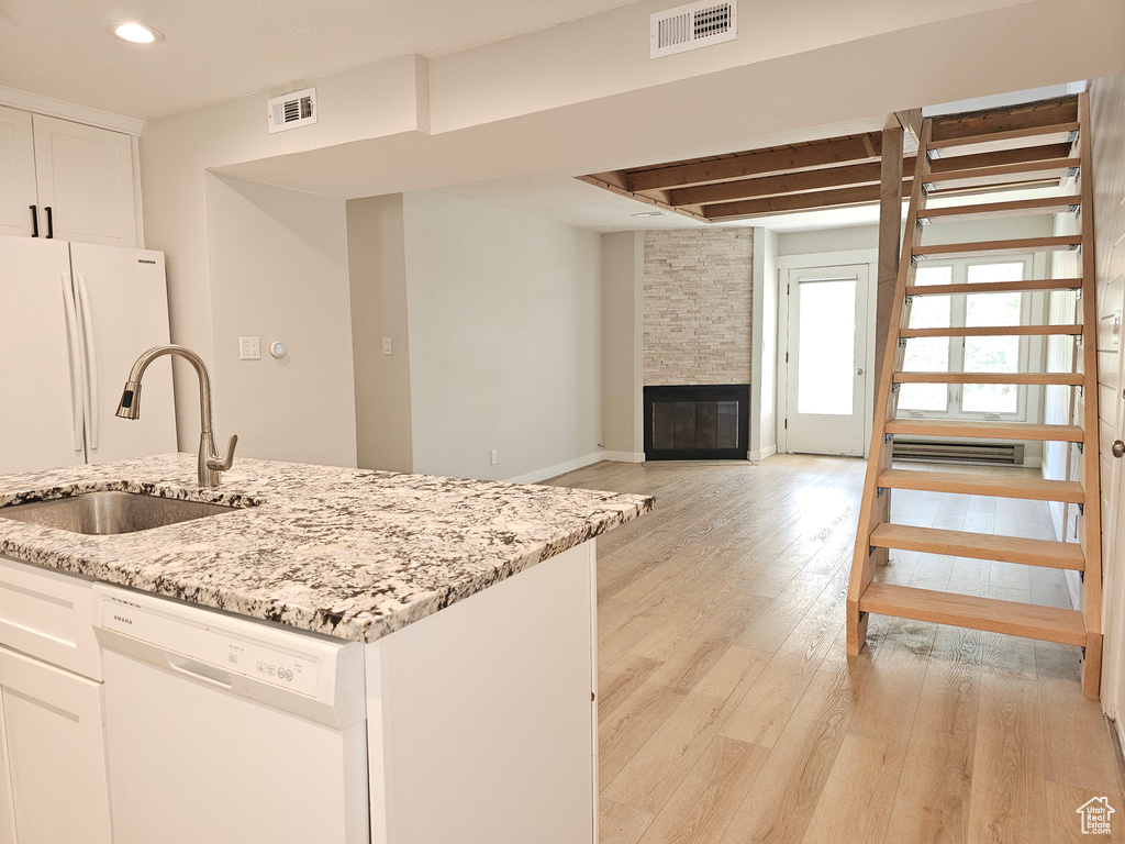 Kitchen featuring white appliances, light wood-style flooring, white cabinets, light stone countertops, and a fireplace