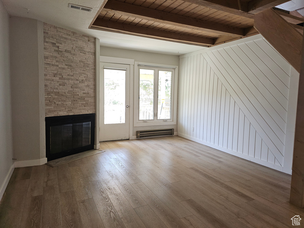 Unfurnished living room featuring baseboard heating, wood finished floors, a stone fireplace, and a wood ceiling with exposed beams