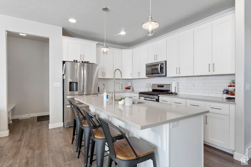 Kitchen featuring appliances with stainless steel finishes, a kitchen bar, decorative backsplash, light countertops, and white cabinets