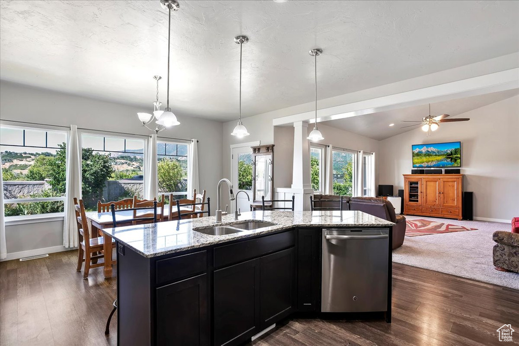 Kitchen with stainless steel dishwasher, open floor plan, dark cabinets, light stone countertops, and vaulted ceiling