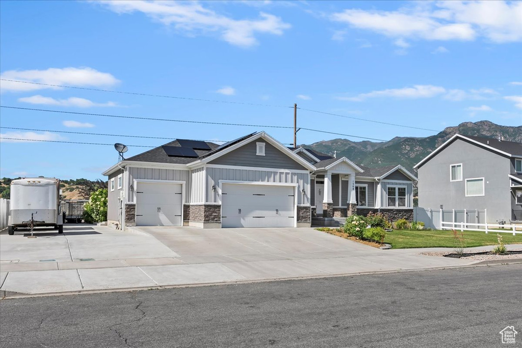 View of front of house with board and batten siding, a garage, a mountain view, roof mounted solar panels, and stone siding