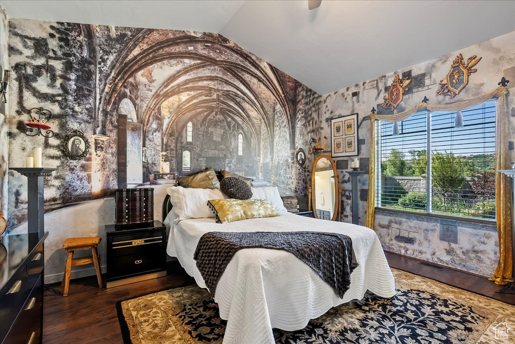 Bedroom featuring vaulted ceiling, wood finished floors, arched walkways, and wallpapered walls