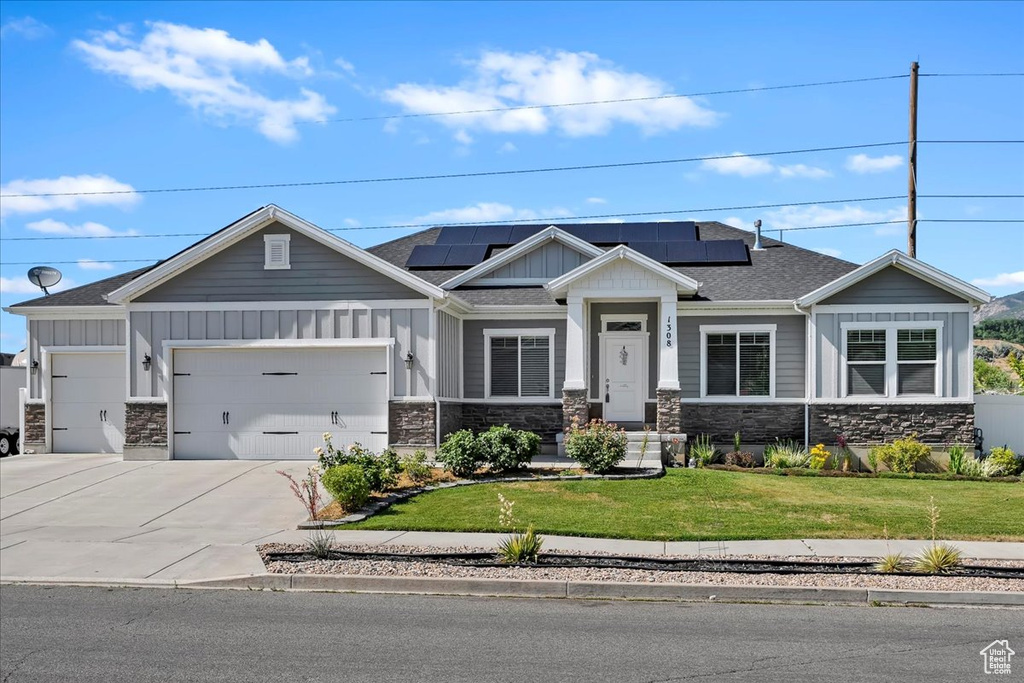 Craftsman-style house with board and batten siding, a front lawn, stone siding, a garage, and driveway