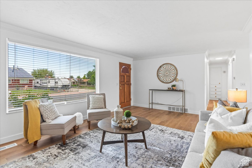 Living room featuring healthy amount of natural light, wood finished floors, and ornamental molding