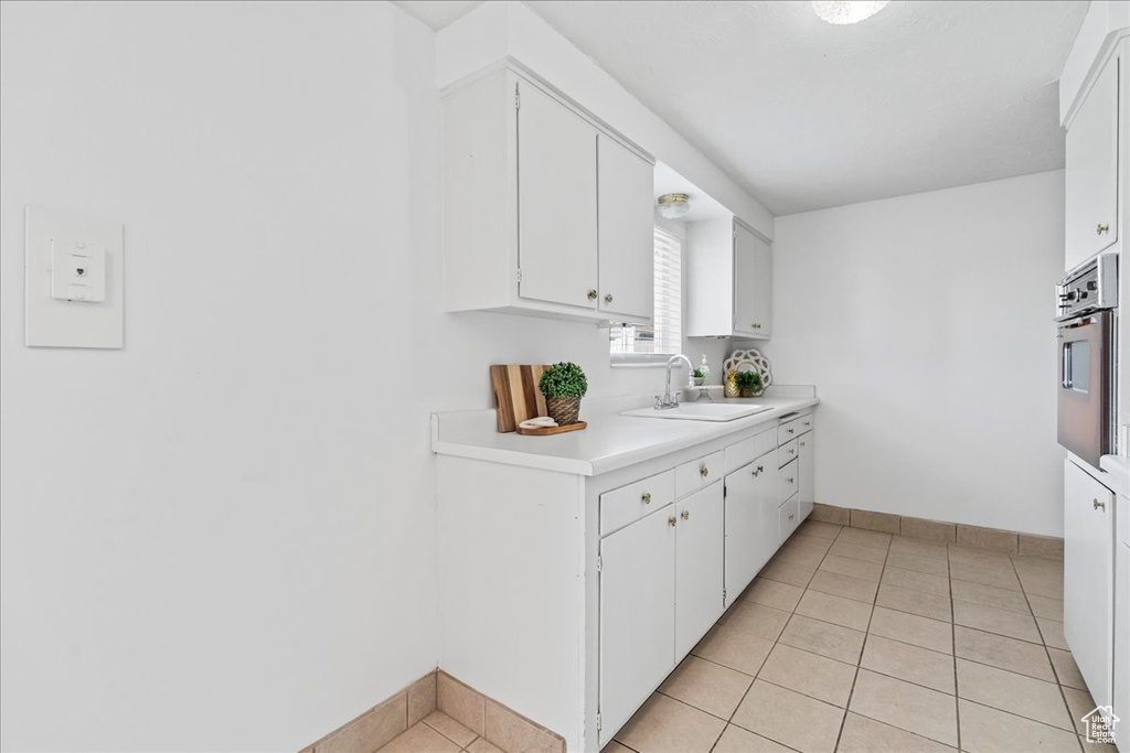 Kitchen with stainless steel oven, white cabinets, light countertops, and light tile patterned floors