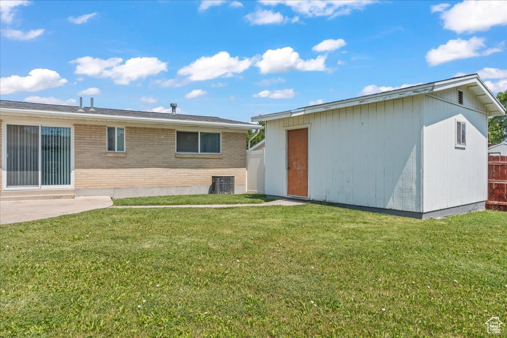 Rear view of house with a lawn, brick siding, and a storage shed