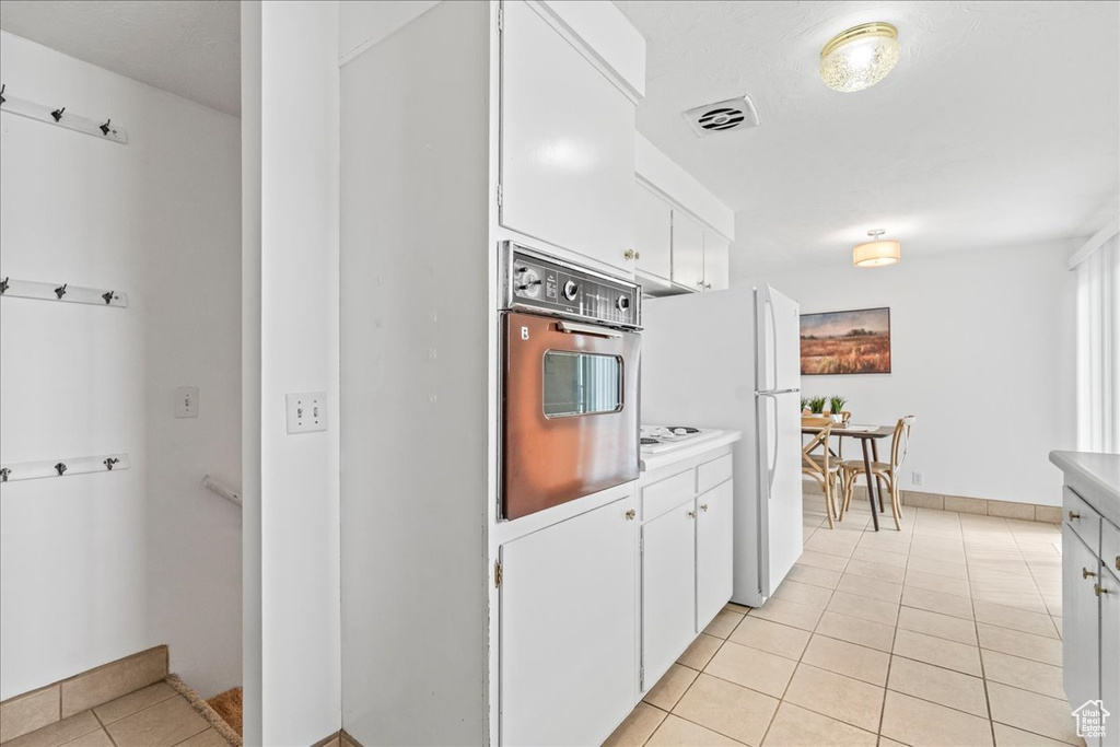 Kitchen with oven, freestanding refrigerator, light tile patterned floors, white cabinetry, and light countertops
