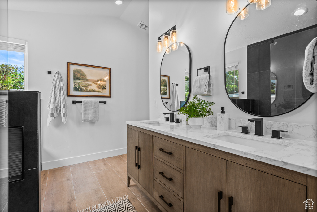 Bathroom with double vanity, wood finished floors, a chandelier, and vaulted ceiling