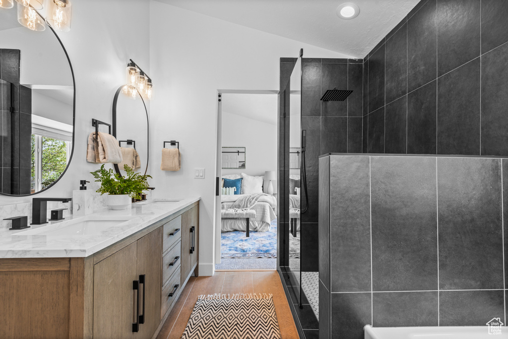 Ensuite bathroom featuring vaulted ceiling, double vanity, wood finished floors, a tile shower, and a tub to relax in