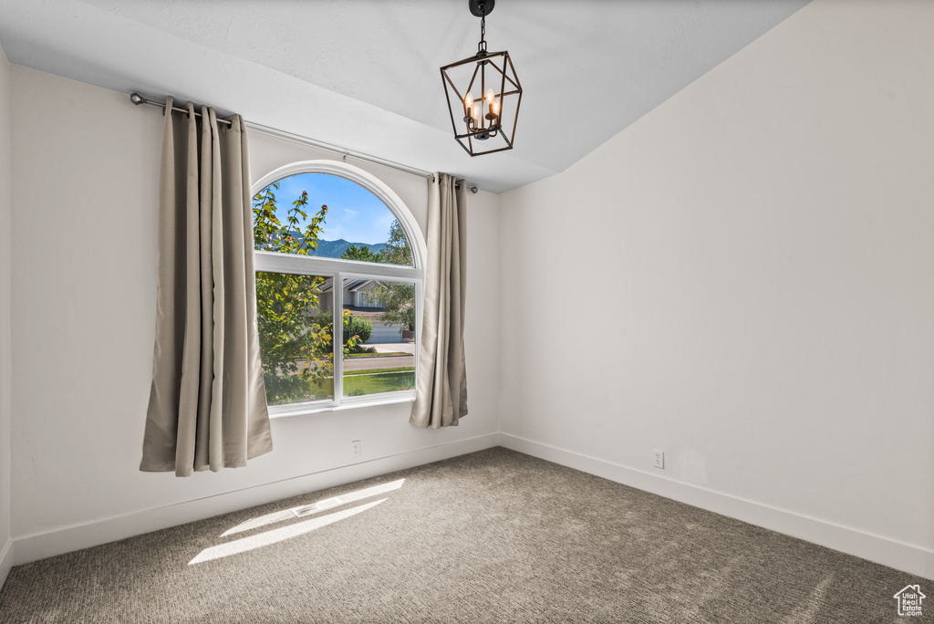 Carpeted empty room with a chandelier and baseboards