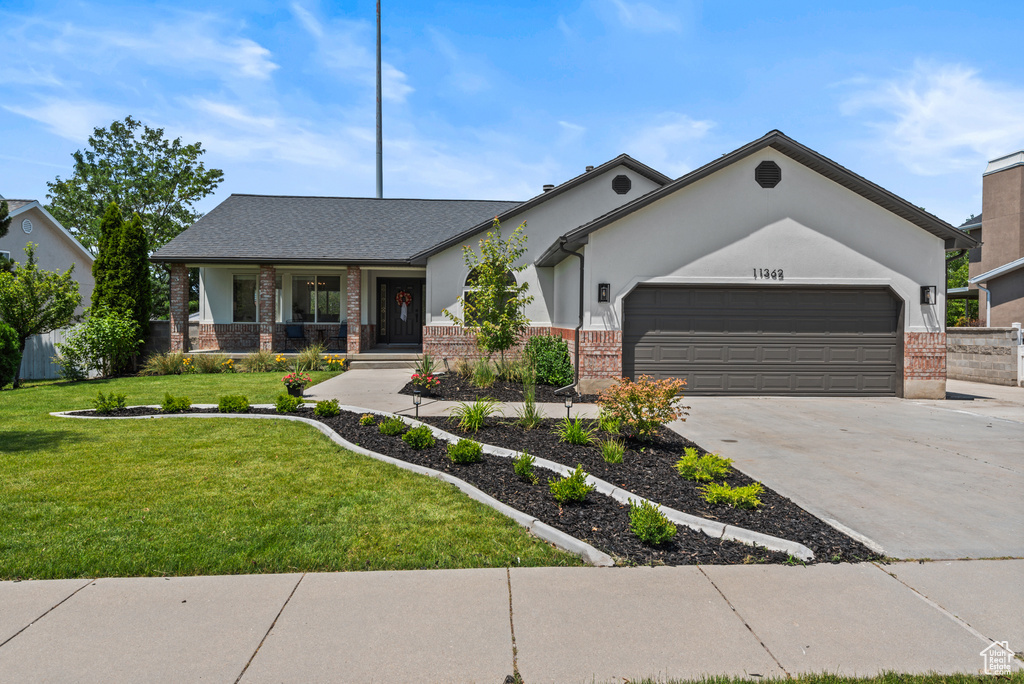 View of front of home featuring brick siding, an attached garage, concrete driveway, covered porch, and a front yard