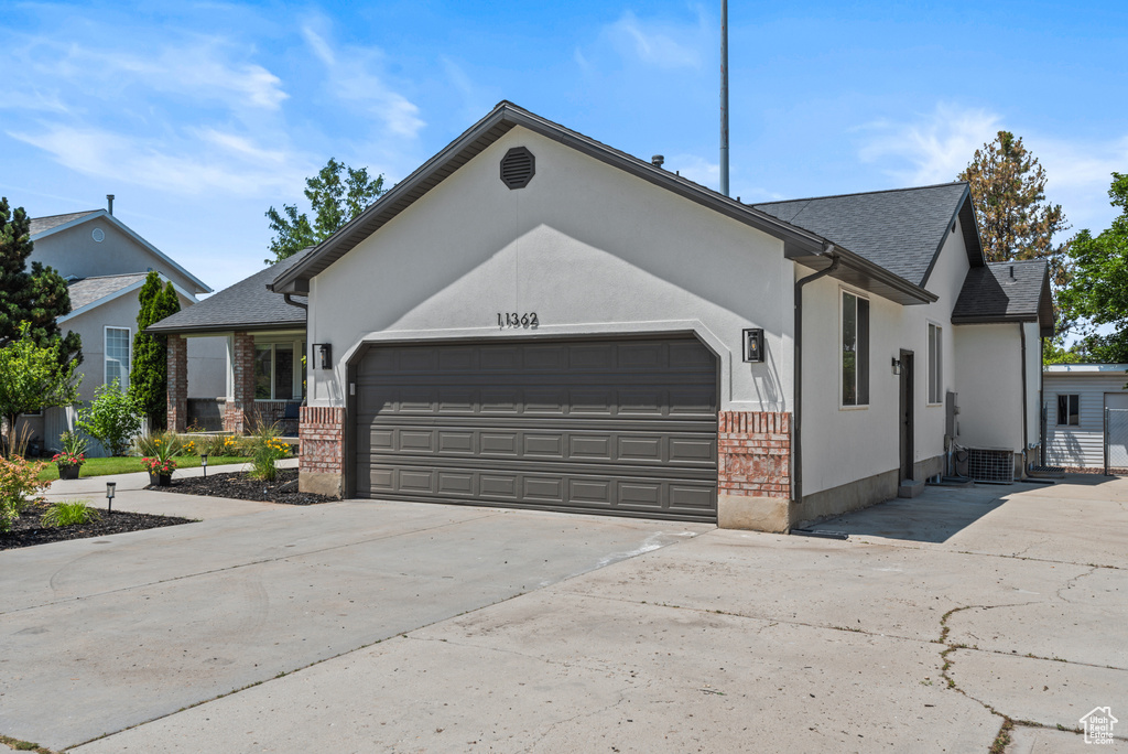 Ranch-style home featuring a garage, driveway, brick siding, a shingled roof, and stucco siding