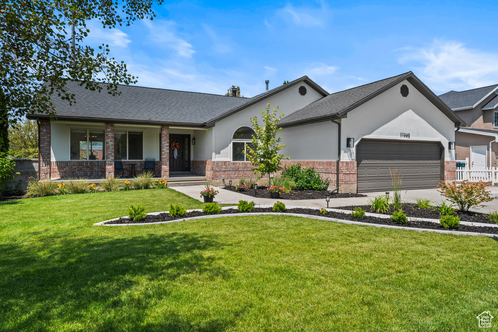 View of front of home with brick siding, an attached garage, covered porch, and a front yard