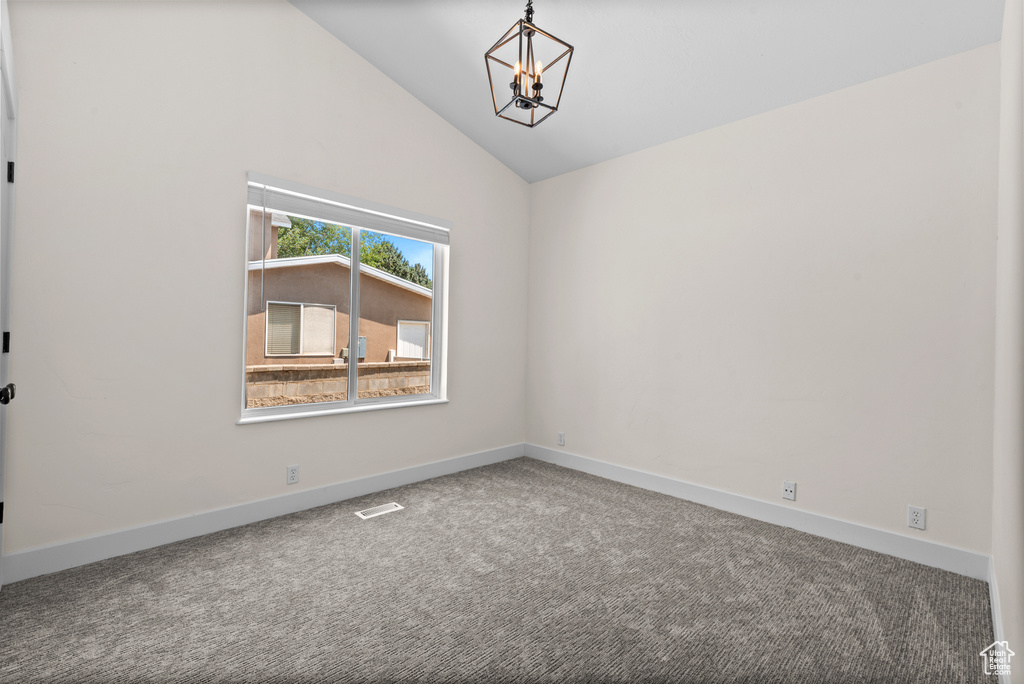 Carpeted empty room featuring a chandelier and lofted ceiling