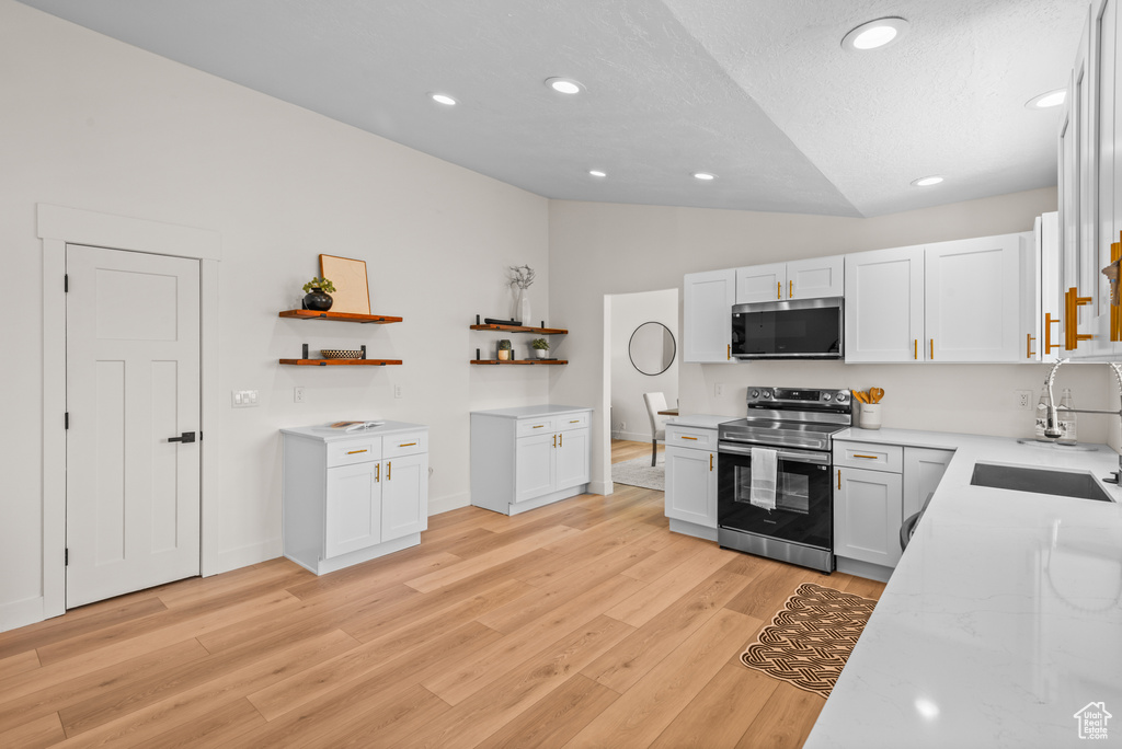 Kitchen with appliances with stainless steel finishes, lofted ceiling, open shelves, light wood-type flooring, and white cabinetry