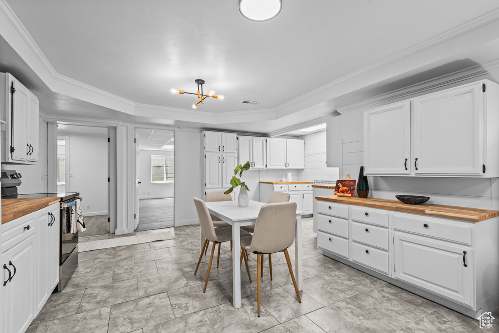 Kitchen with butcher block counters, stainless steel range with electric cooktop, a chandelier, white cabinetry, and ornamental molding