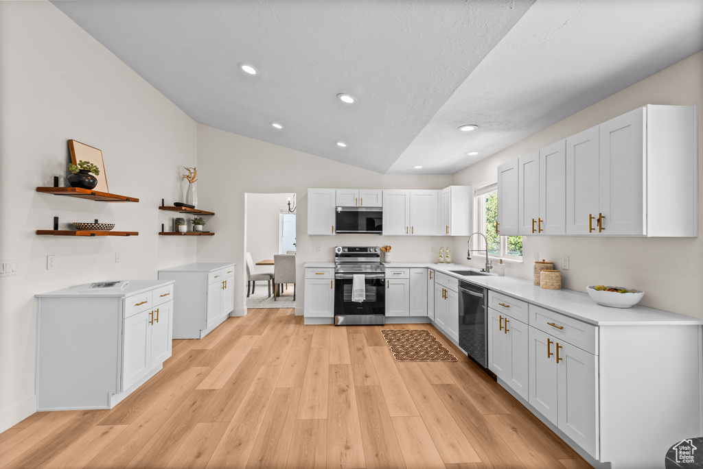 Kitchen with stainless steel appliances, open shelves, light wood-style flooring, vaulted ceiling, and light countertops