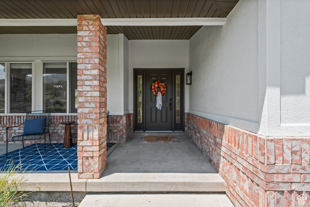 View of exterior entry with covered porch, brick siding, and stucco siding