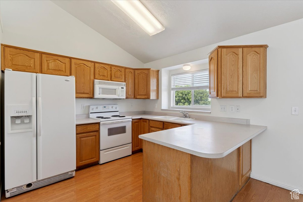 Kitchen featuring white appliances, vaulted ceiling, a peninsula, light wood finished floors, and light countertops