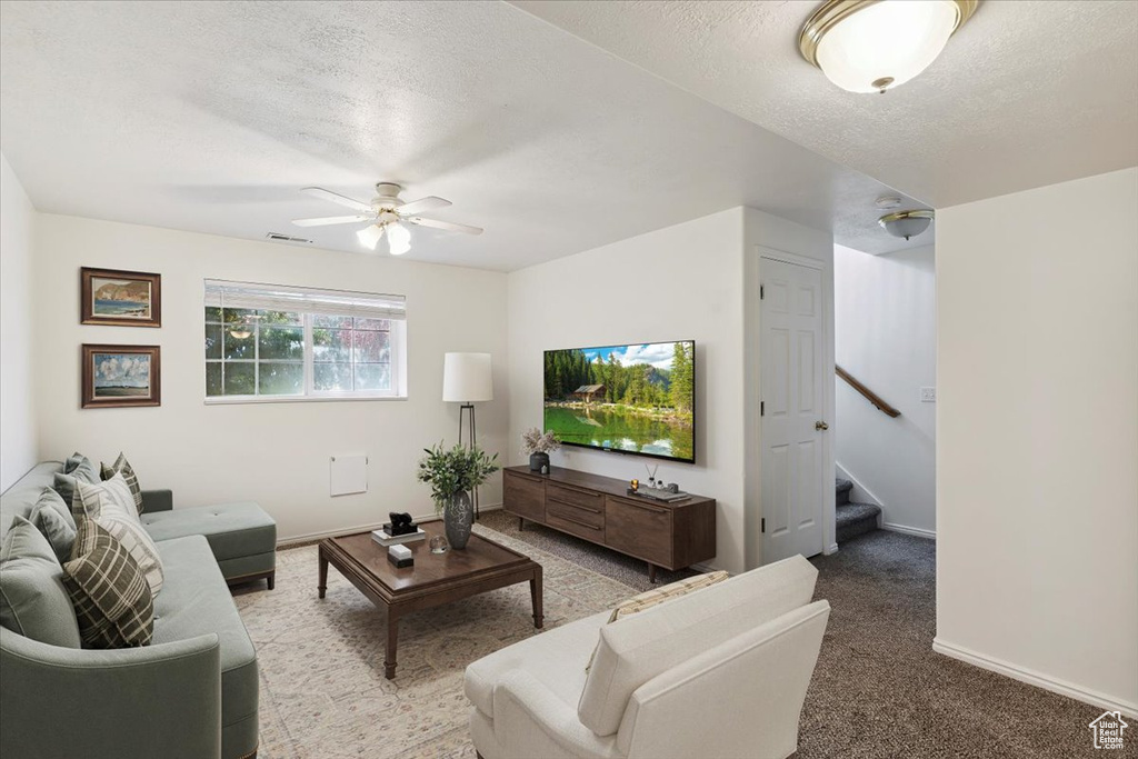 Living area with a ceiling fan, a textured ceiling, carpet, and stairs