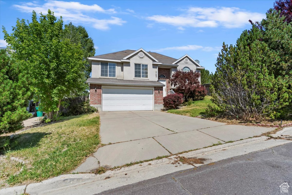 Traditional home with driveway, an attached garage, brick siding, and a front yard