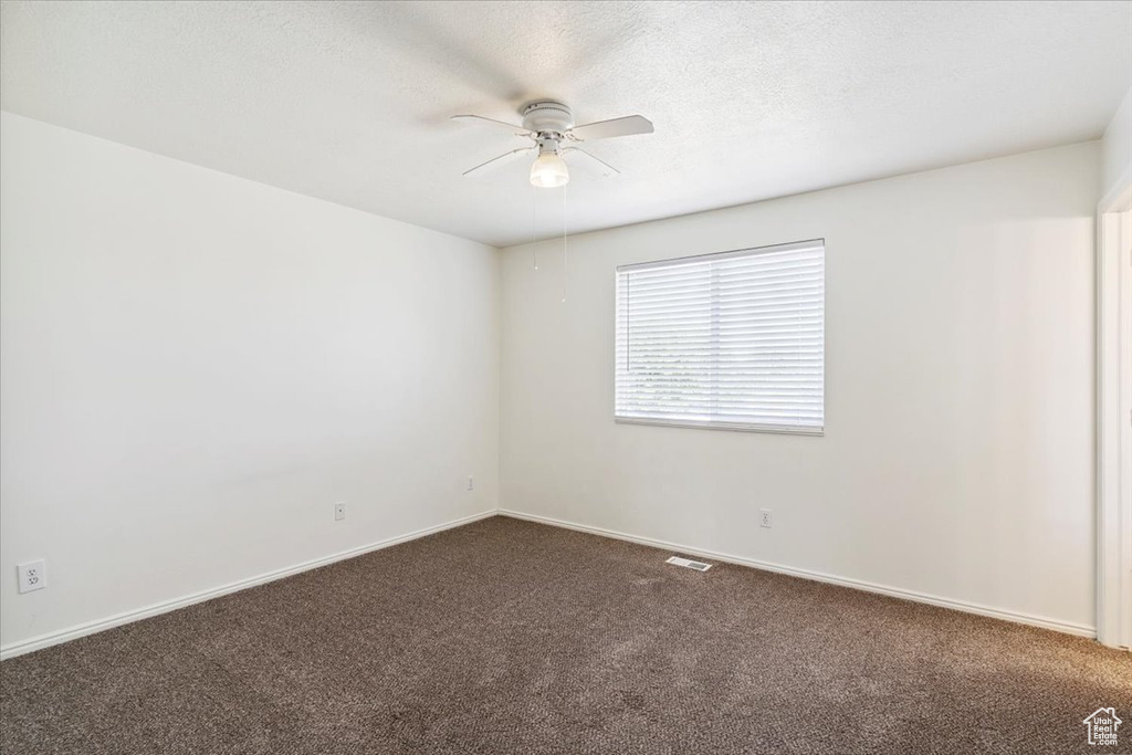 Empty room featuring dark carpet and ceiling fan
