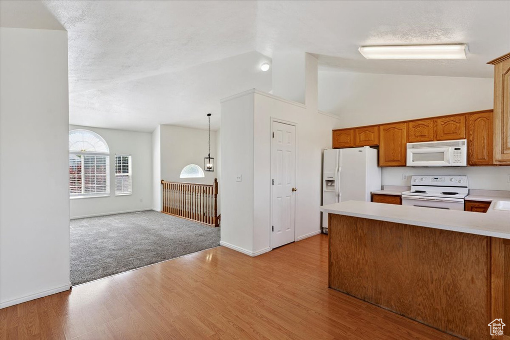 Kitchen featuring white appliances, a peninsula, light countertops, light wood-style floors, and brown cabinets