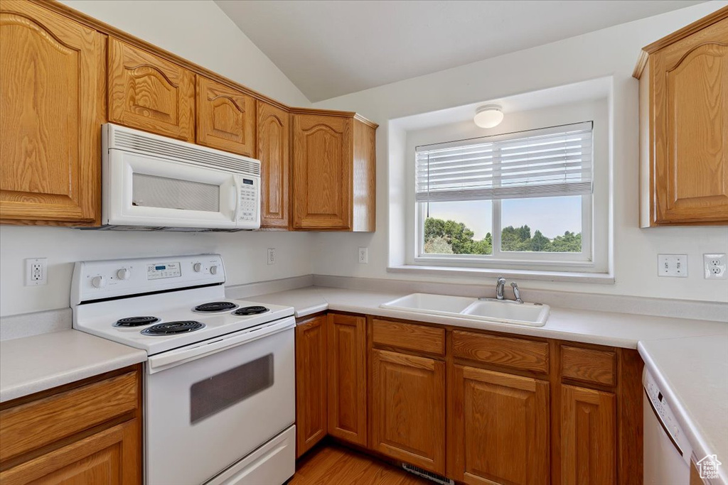 Kitchen featuring white appliances, lofted ceiling, light countertops, and brown cabinetry