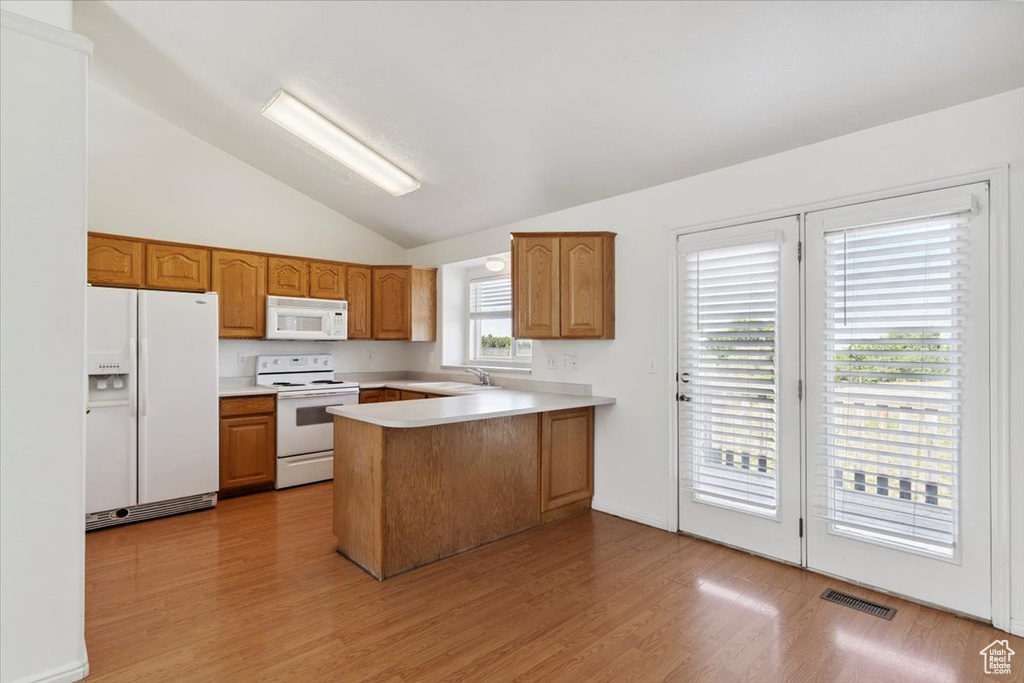 Kitchen with white appliances, a peninsula, lofted ceiling, light countertops, and brown cabinets