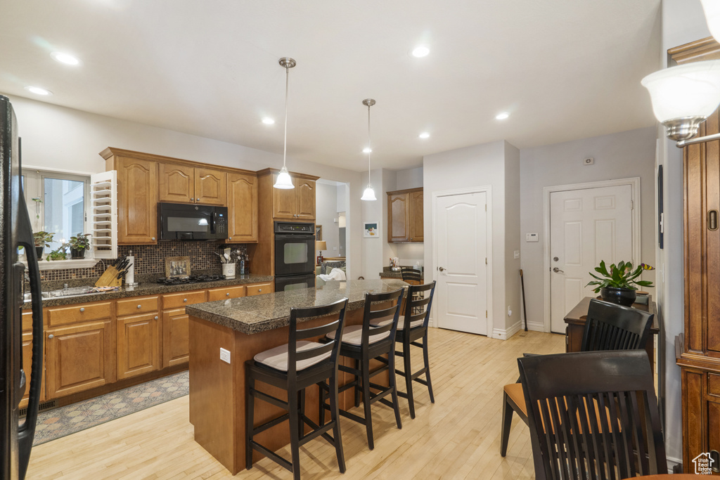 Kitchen with black appliances, a kitchen island, light wood-type flooring, decorative backsplash, and recessed lighting