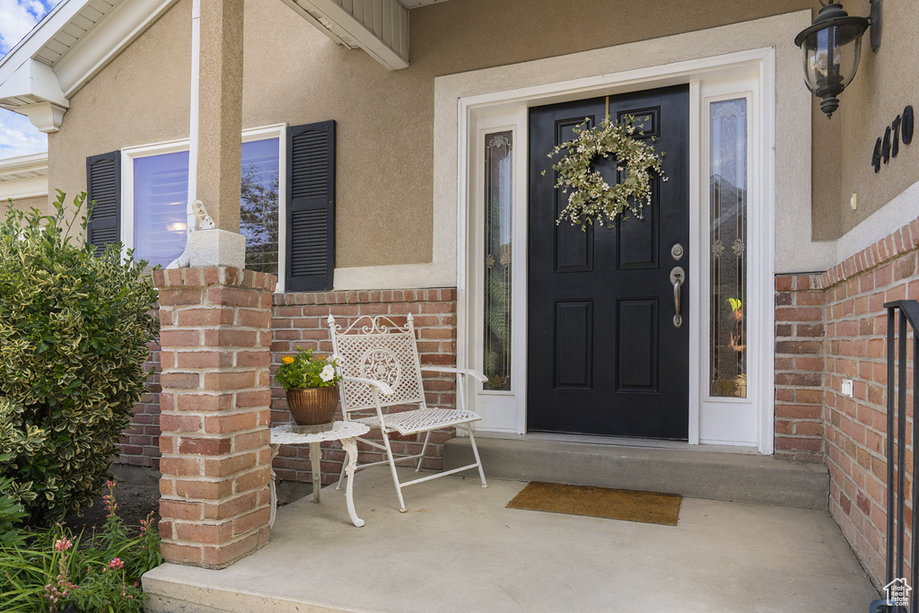 Entrance to property with stucco siding, brick siding, and a porch