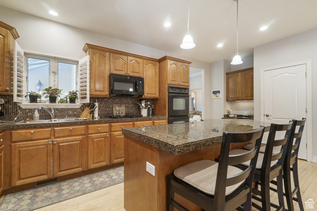 Kitchen with black appliances, light wood-style floors, a kitchen island, decorative backsplash, and recessed lighting